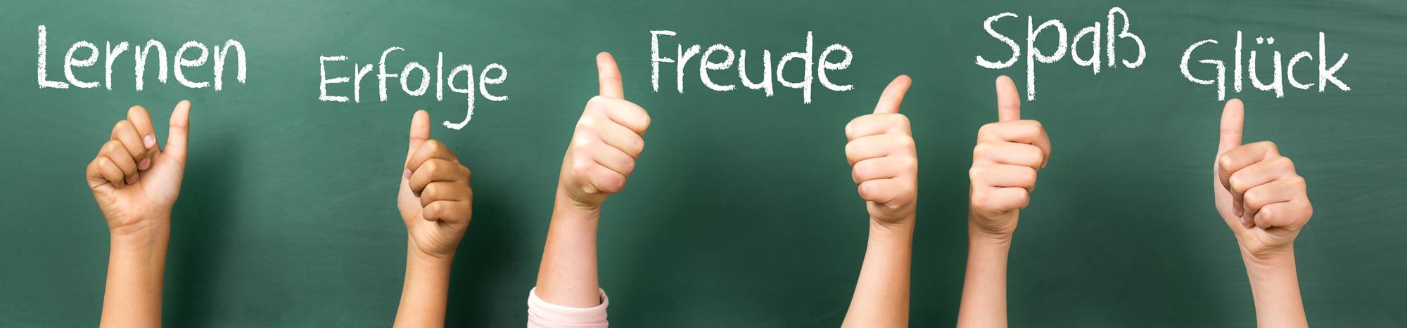 Kinderhände schreiben mit Kreide Befriffe an eine grüne Tafel: Lernen, Erfolge, Freude, Spaß, Glück